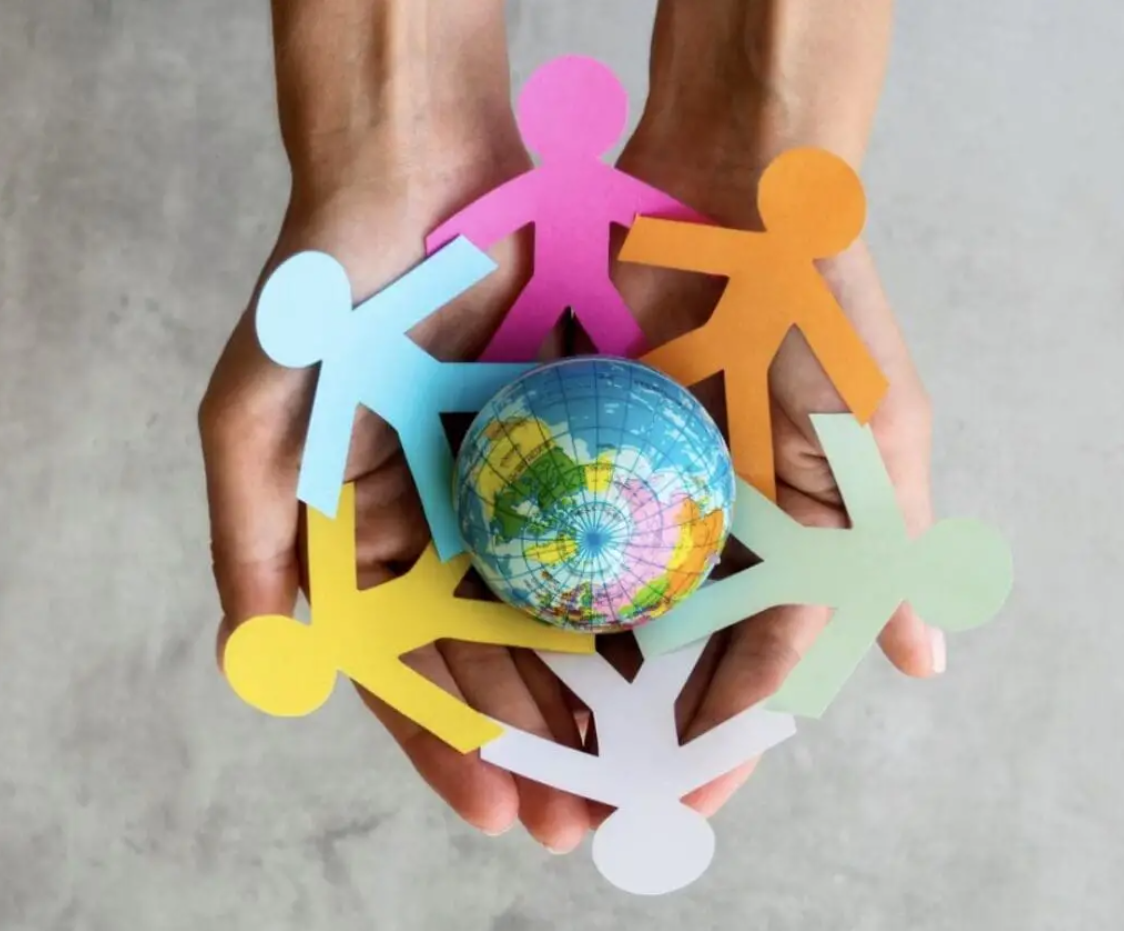 Multicolored cutouts of people surrounding a small globe in the palm of someone's hands